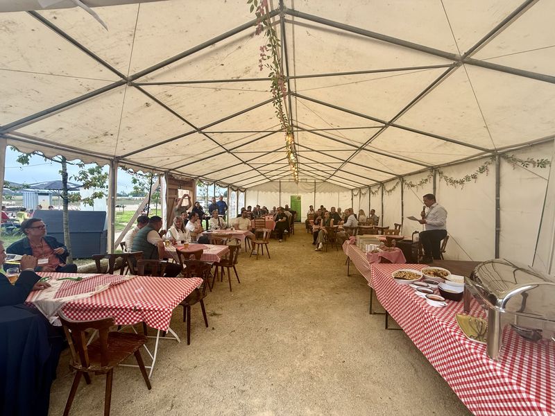 Blick durchs Festzelt beim Unternehmer-BBQ: gedeckte Tische mit karierten Decken, die ersten Gäste kommen an.